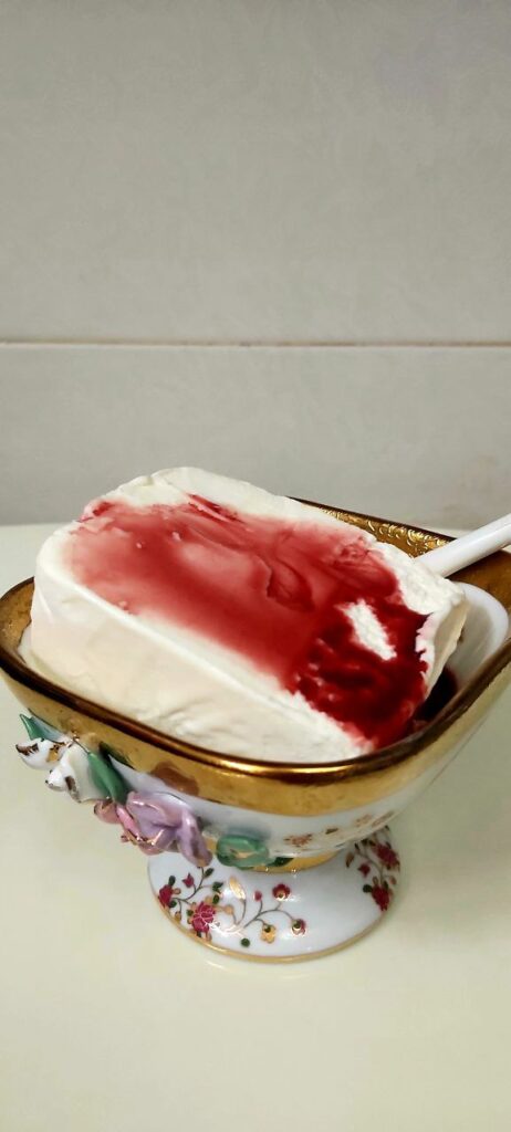 Close-up of traditional Persian Bastani Sonnati ice cream topped with sweet cherry syrup, served in an elegant stemmed Chinese ice cream bowl. Garnished with pistachios