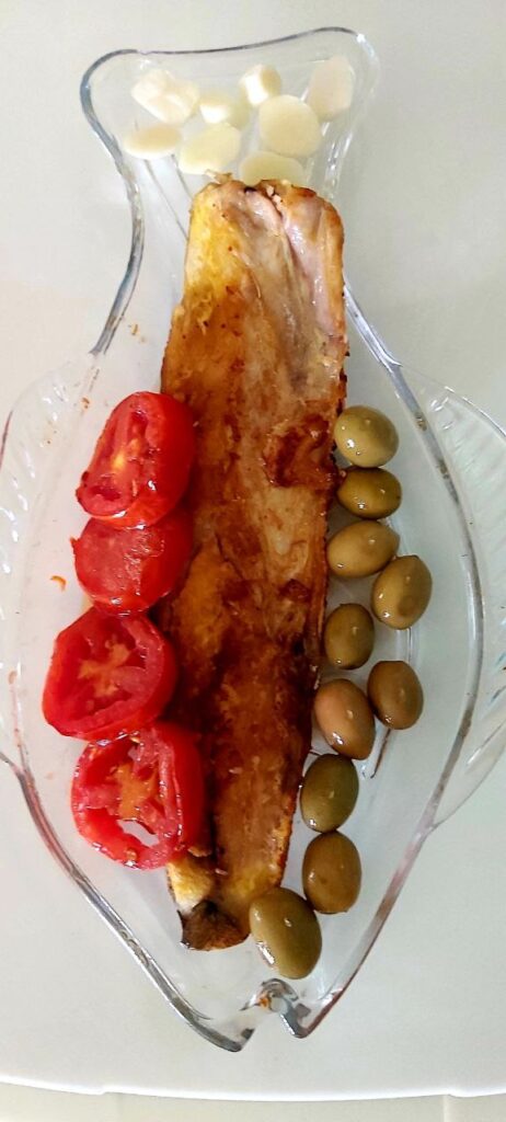 Fish-shaped crystal dish with grilled salmon, olives, and fried tomatoes.