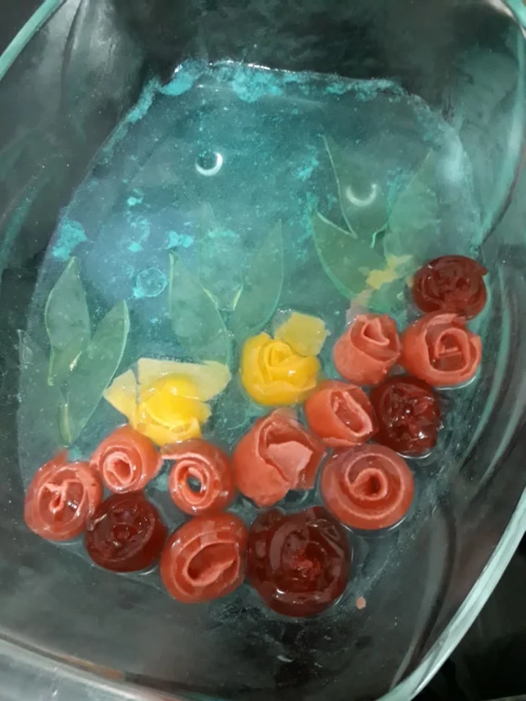 Blue-green jelly in a crystal dish with colorful rose-shaped jelly flowers on top.