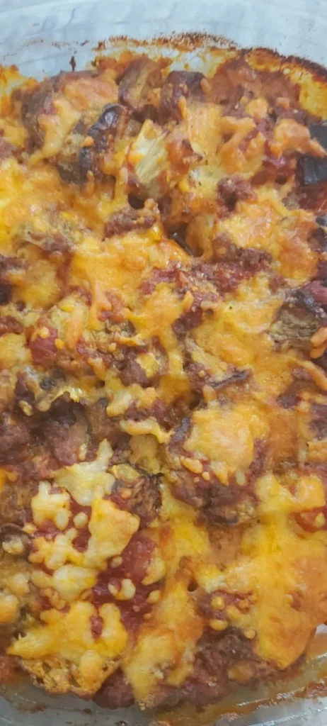 Peeled and sliced eggplant, fried and layered in a clear rimmed glass dish. Each layer is topped with sautéed onions, minced meat, and melted pizza cheese. The dish is served warm in a transparent glass baking dish with visible golden cheese on top.