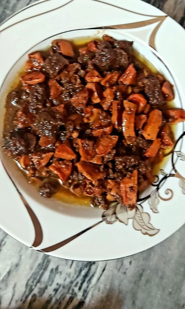 A close-up of Persian quince stew (Khoresh-e Beh) with tender lamb pieces and golden sliced quince in a rich, tomato-based sauce on a white plate.