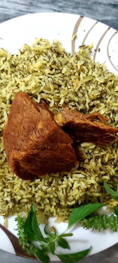 Persian dill rice with two large pieces of meat, served on a white porcelain plate with fresh basil leaves.