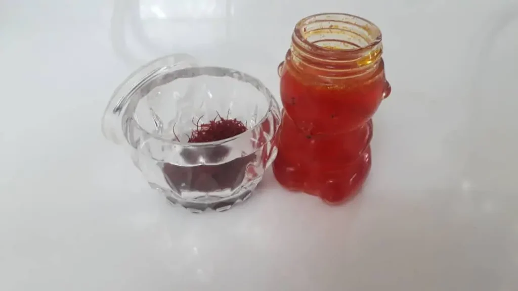Close-up of liquid saffron in a small glass jar next to premium-grade saffron threads in a clear container