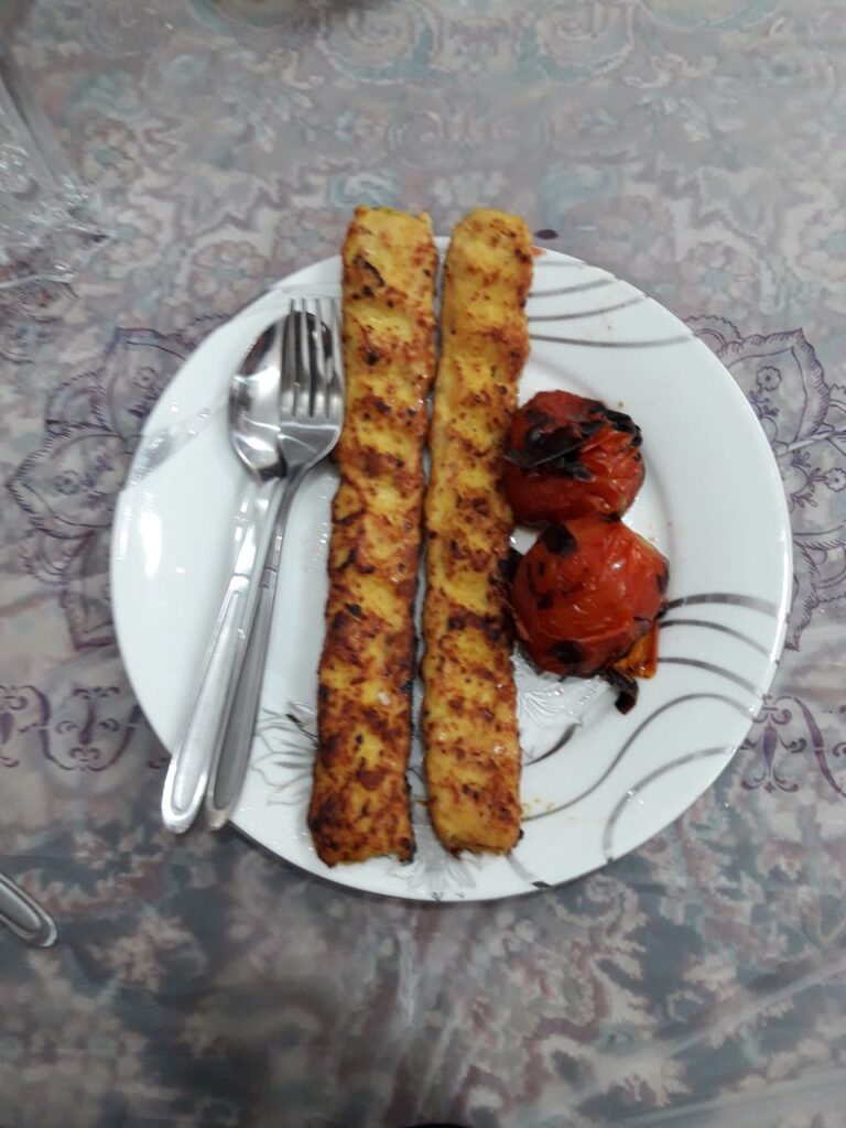 Chicken kebabs served on a white porcelain plate with a fork and spoon placed beside them.