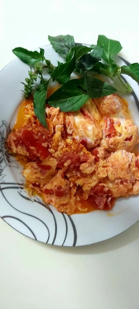 A fluffy homemade omelette served on a traditional Chinese plate with fresh basil leaves on the side