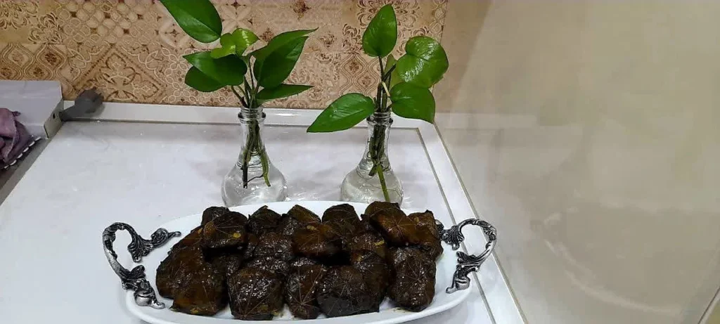 White Chinese dish with Dolma Barg Moo, accompanied by colored glass vases holding Pothos flower branches.