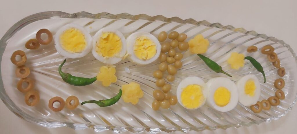 A crystal dish filled with sliced boiled potatoes and boiled eggs, garnished with green pepper and a sprinkle of salt.