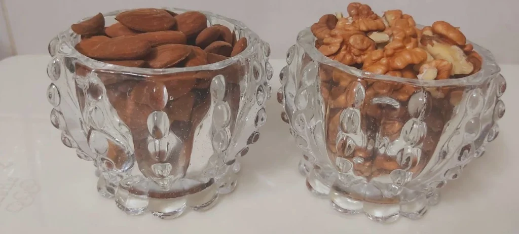 Two small crystal bowls, one filled with almonds and the other with walnuts.