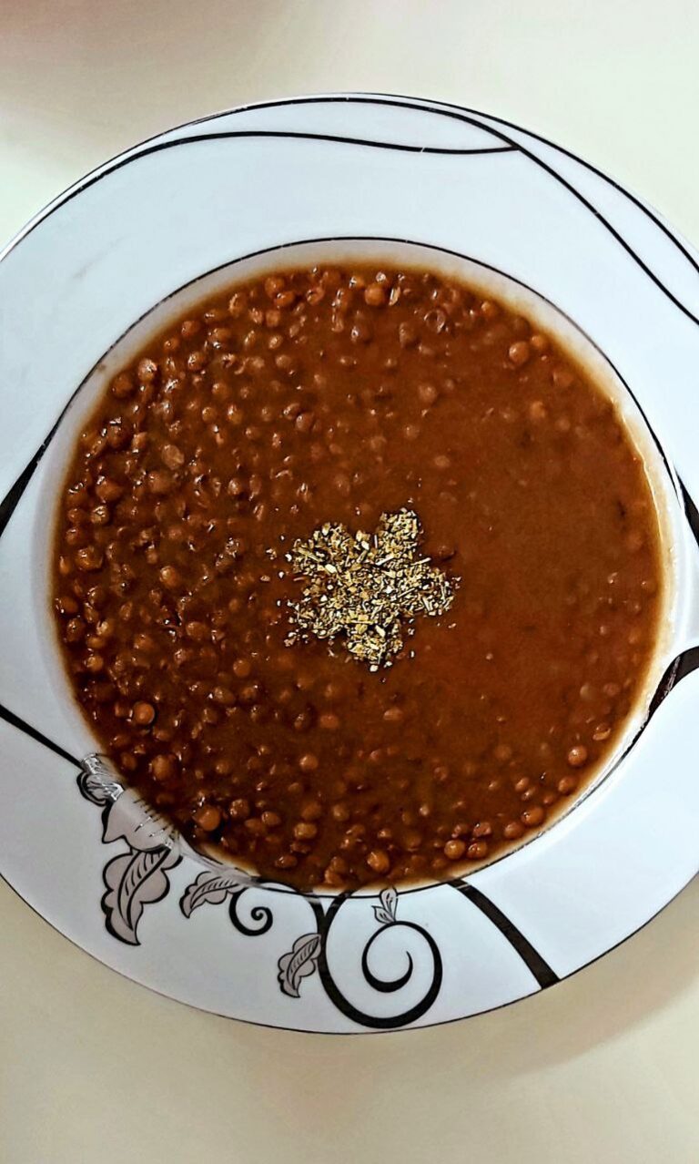 A white porcelain plate of cooked lentils garnished with angelica leaves.