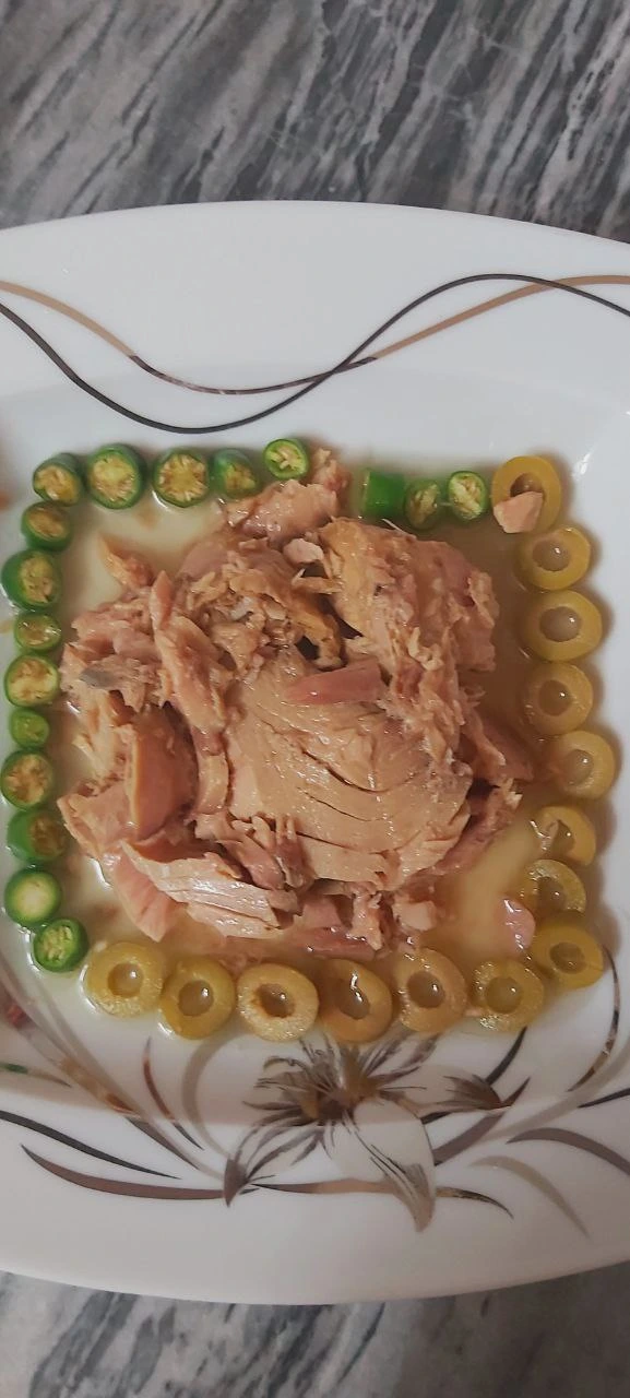 A white porcelain plate containing a serving of tuna surrounded by olives and sliced peppers, is presented as a healthy meal option.