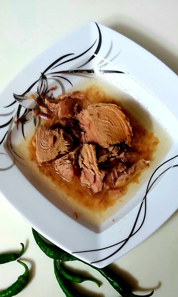 A square Chinese plate with tuna, surrounded by fish oil and garnished with green peppers beside the plate.