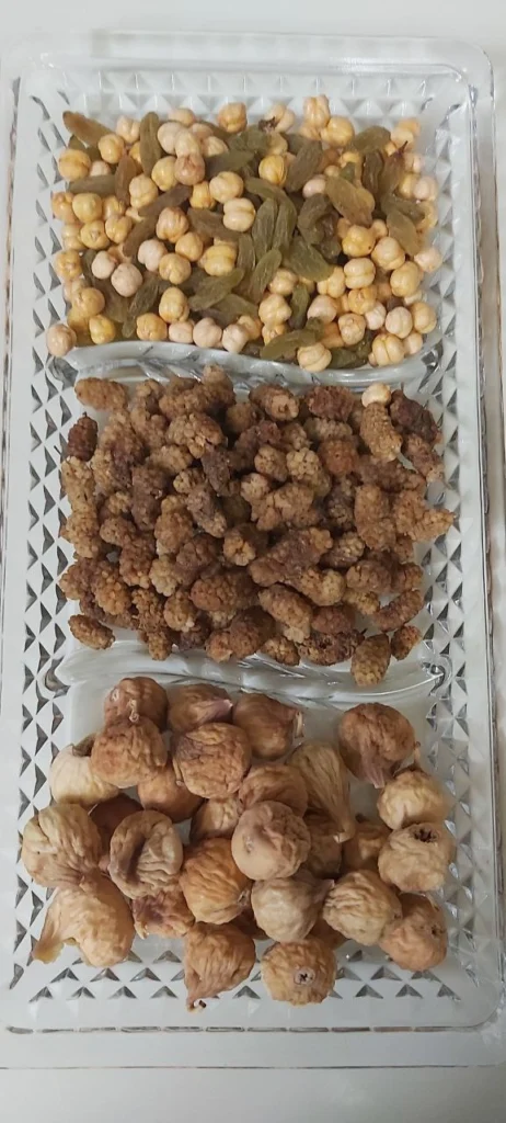 Closeup photo of a rectangular glass dish with three sections containing raisins, roasted chickpeas, dried dried berries, and dried figs