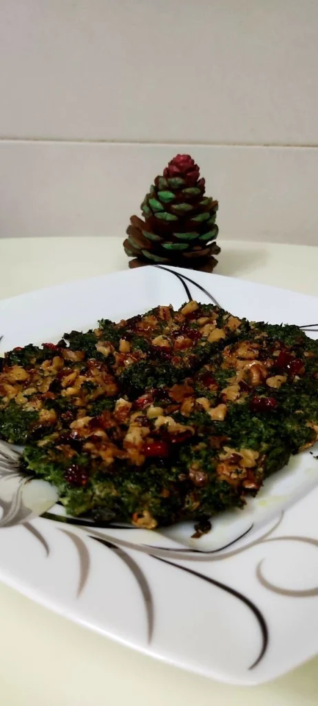 A square Chinese plate with a vegetable coco appetizer topped with walnuts and barberries, alongside a green and brown pine cone.