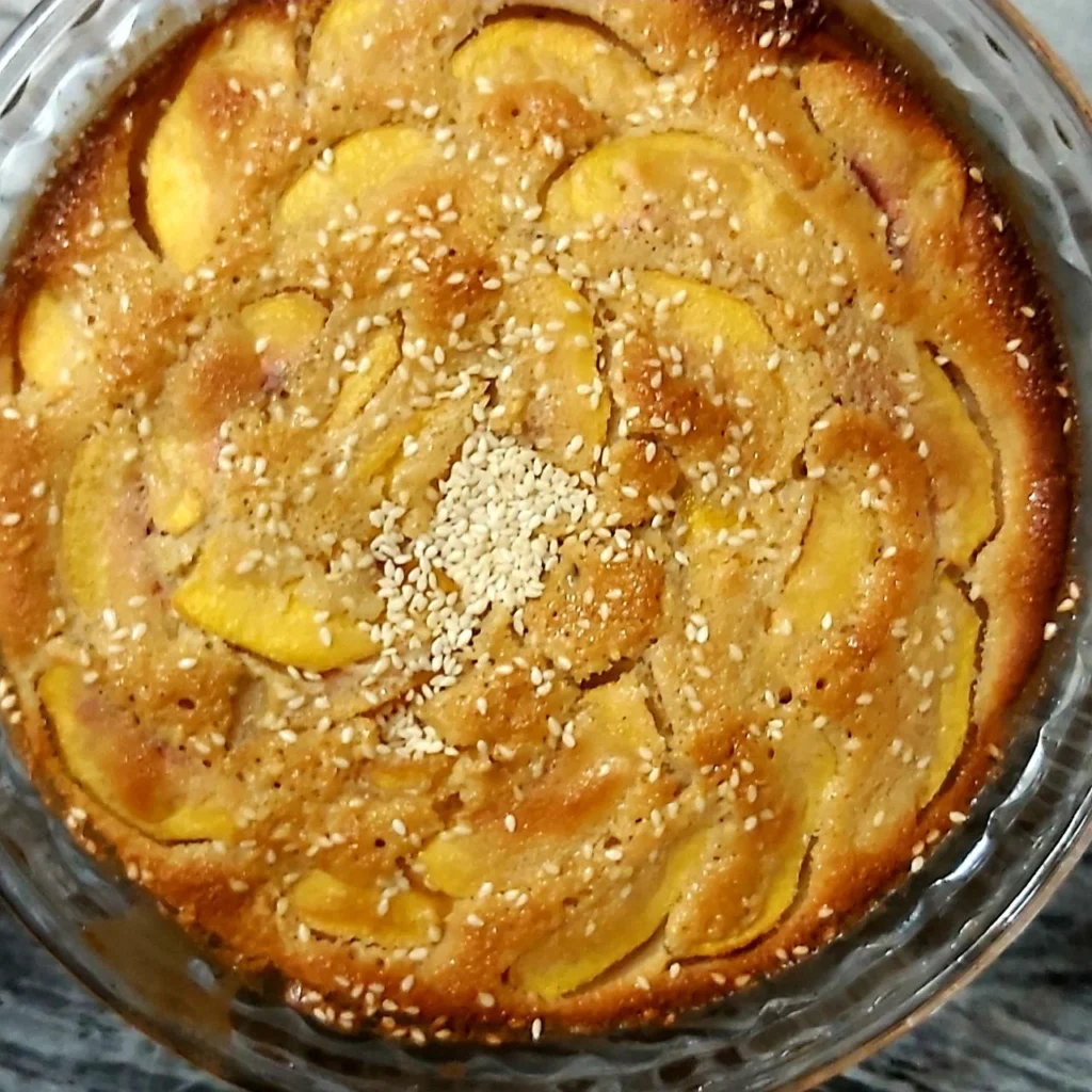 Peach cake in a round Pyrex dish with neatly arranged peach slices on top