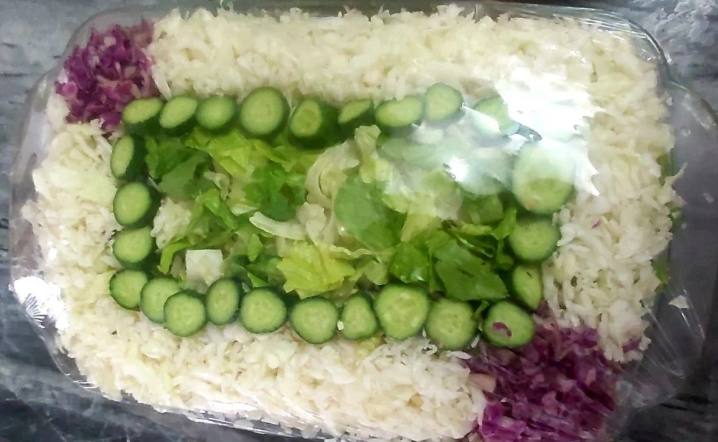 Rimmed Pyrex dish with chopped lettuce, garnished with white and red cabbage and cucumber slices.