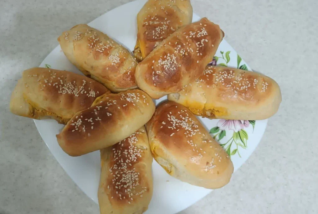 Eight sesame sandwich breads arranged on a white plate decorated with a purple flower and green leaf design.