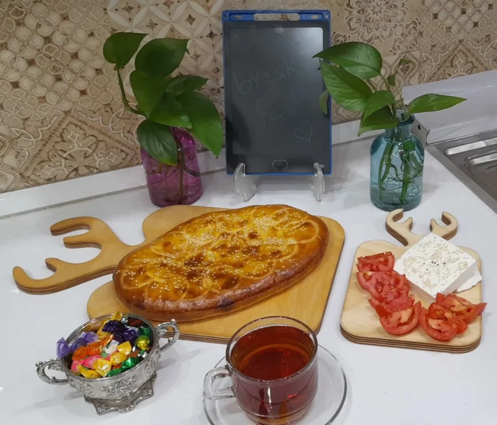 A delicious breakfast featuring unleavened bread on a stick, served with slices of cheese and fresh tomatoes, accompanied by a cup of tea. Two elegant blue and purple glass vases hold vibrant pothos flowers, adding a touch of greenery to the table setting.