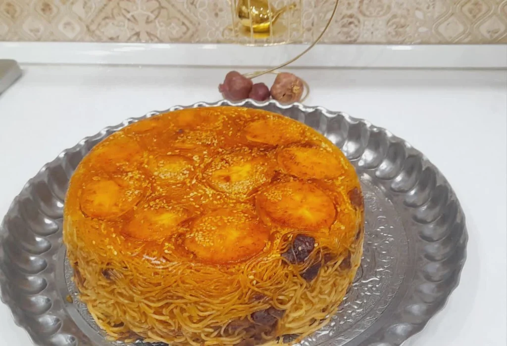 A molded Persian-style pasta topped with a golden crispy potato crust, served as a cake-like dish.