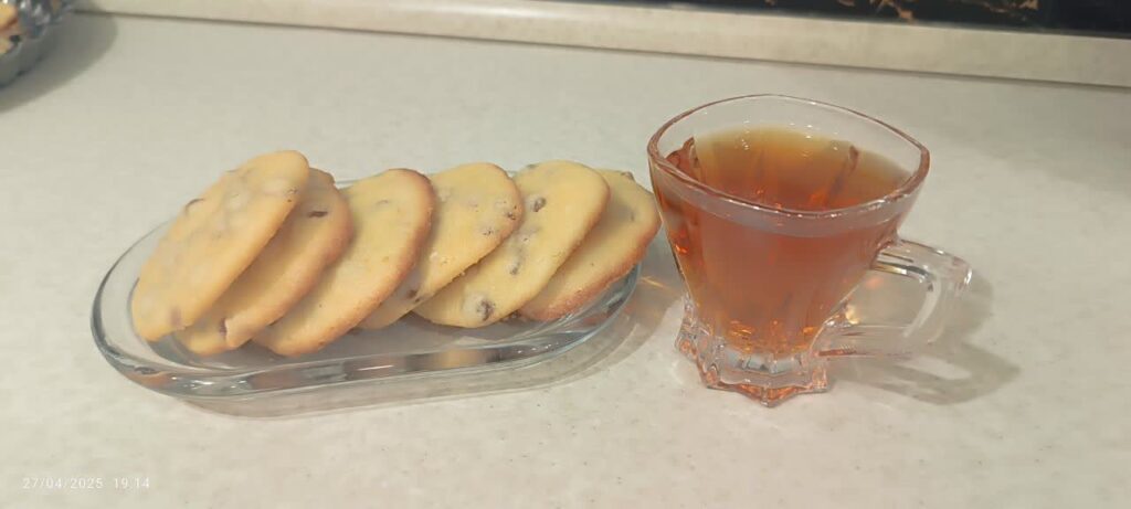 A Crystal bowl filled with raisin cookies next to a glass of tea.