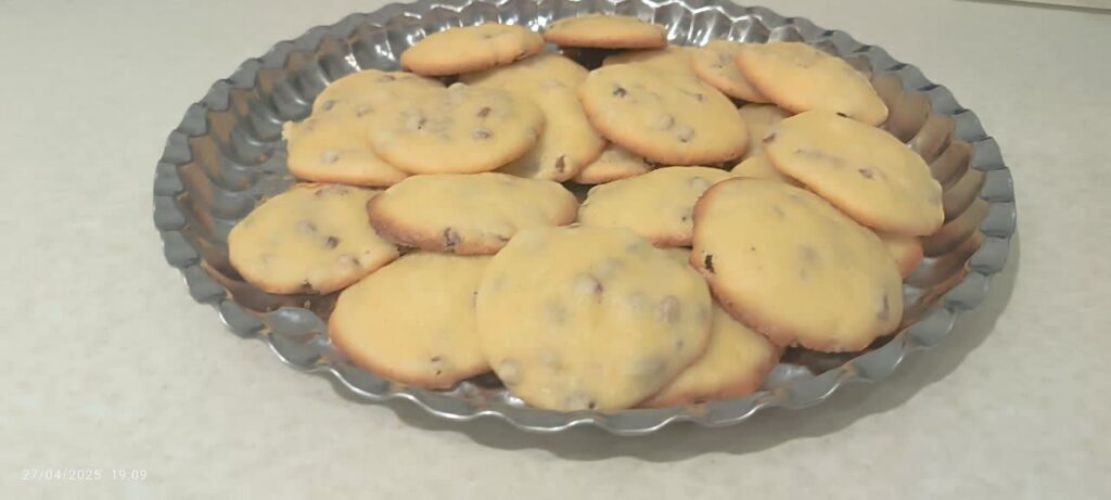 Steel plate filled with freshly baked, golden brown raisin cookies.