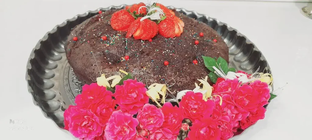 Decorated chocolate cake surrounded by purple flowers and topped with fresh strawberries"