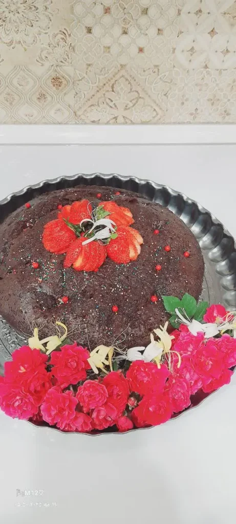 Moist chocolate cake in round metal tray with strawberry slices and white edible flowers