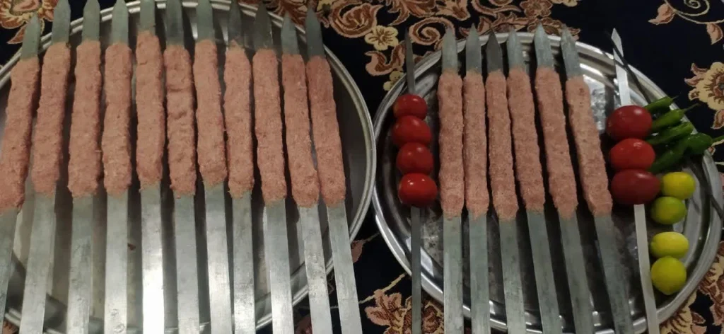 Raw minced meat skewers with lemons, green peppers, and tomatoes prepared for Koobideh kebab.