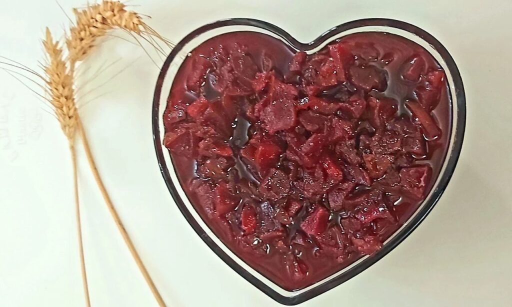Homemade quince jam in a heart-shaped glass jar with two dried yellow wheat stalks beside it