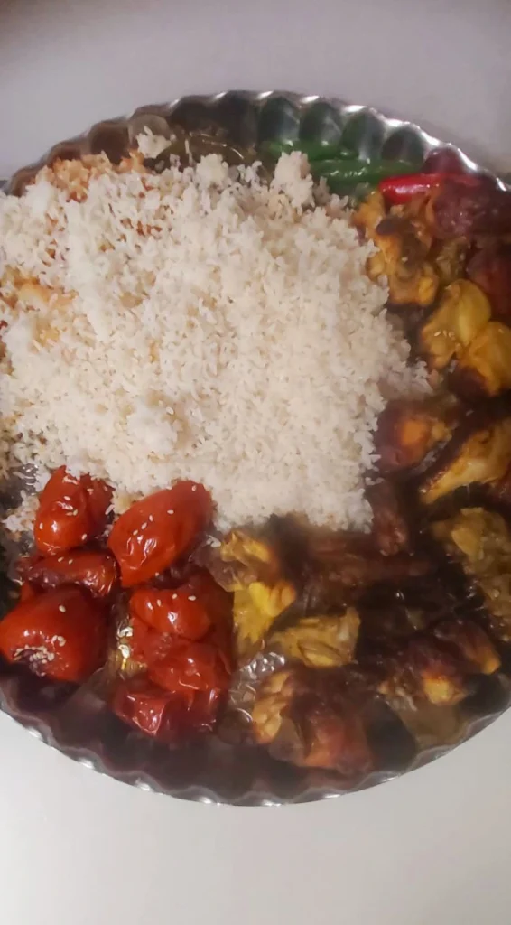 Round stainless steel dish with saffron rice, grilled chicken kebab, roasted tomato, and green pepper