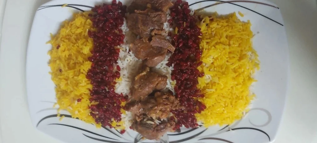White platter with Chelo Gosht, showing saffron rice, barberries, white rice, and lamb shank in the center