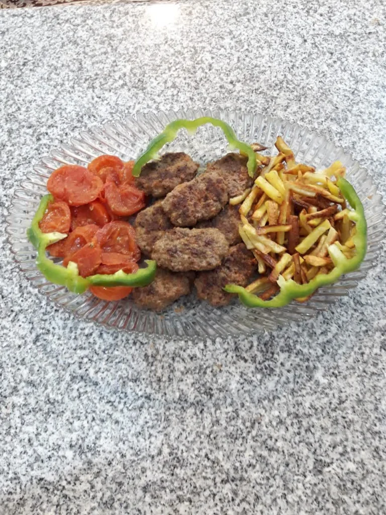 A platter filled with crispy, golden-brown cutlets, alongside perfectly fried potato sticks, vibrant sautéed tomatoes, and colorful chopped bell peppers, arranged artfully for a delicious meal.