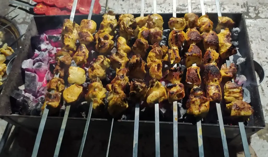 Chicken kebab skewers grilling over charcoal on a metal barbecue grill.