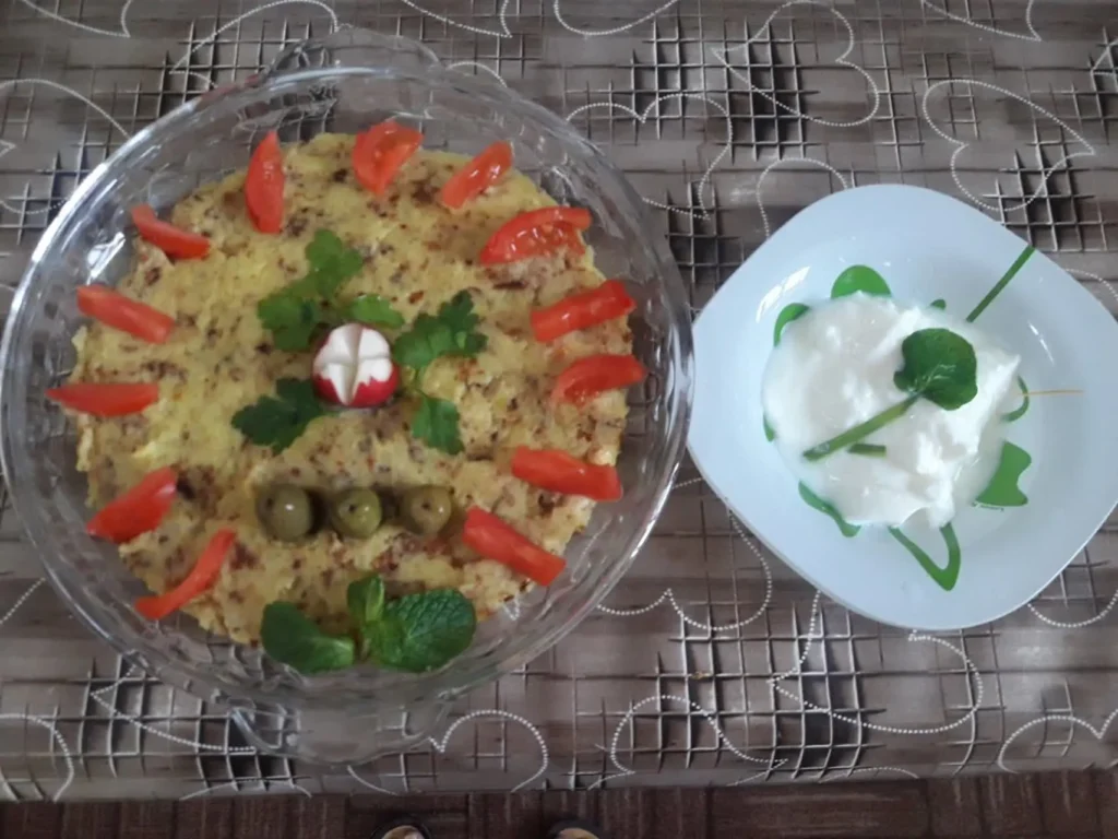 Mashed potatoes and ground beef served on a plate, topped with radish slices, olives, and tomatoes as garnish.