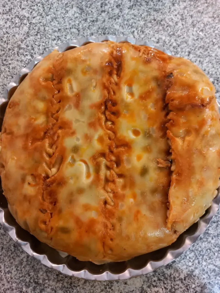 A round, golden-brown baked lasagna with melted cheese in a stainless steel baking dish.