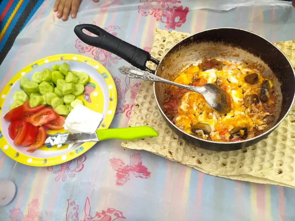 Mushroom omelet in a pan, served with a side plate of cucumber, tomato, and white cheese.
