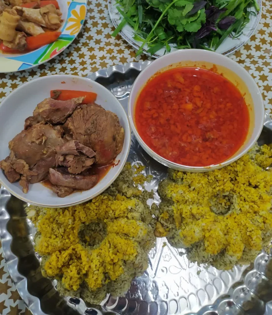 Persian serving tray with a bowl of broth, a bowl of tender meat, and two saffron-decorated dill rice molds.