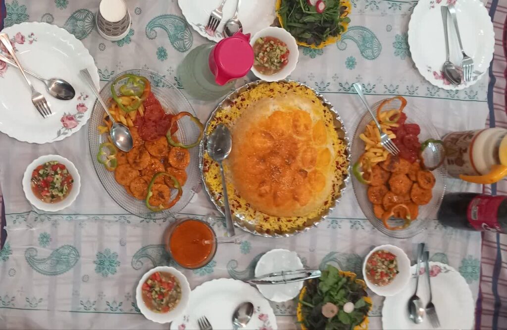A beautifully served dinner table with rice, crispy chicken cutlets, fresh salad, herbs, and refreshing drinks