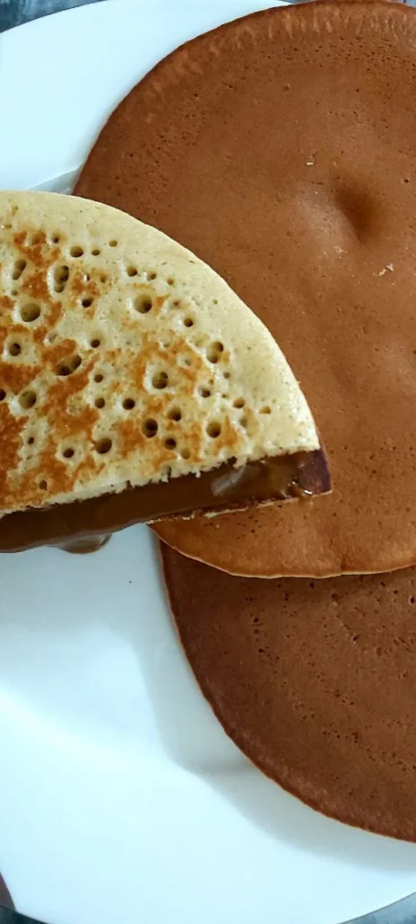 A golden brown pancake with another pancake cut in half on top, showing a gooey chocolate sauce filling.